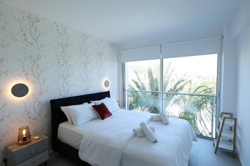 Schlafzimmer mit einem weißen Bett und einem großen Fenster in der Unterkunft Lovely cozy one bedroom suite with pool in Protaras
