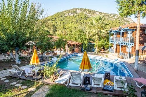 uma piscina com cadeiras e guarda-sóis em frente a uma casa em Olympos Çınar Hotel em Olympos