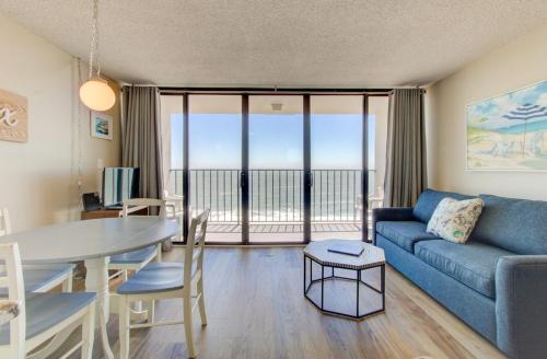 a living room with a blue couch and a table and a dining room at 1010 Relax, Unwind, Enjoy by Atlantic Towers in Carolina Beach