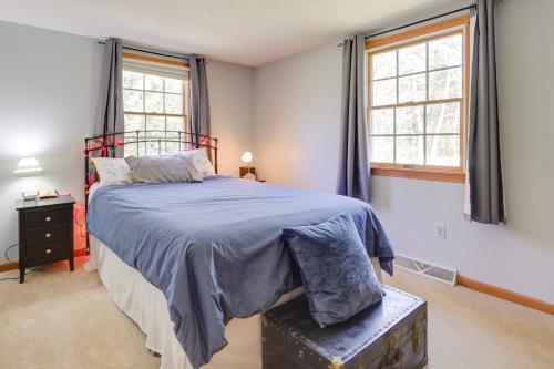 a bedroom with a bed with a blue blanket and two windows at Picturesque Barnstable Rental with Deck and Backyard! in Barnstable