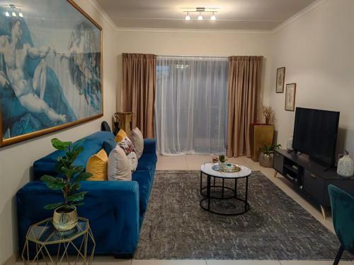 a living room with a blue couch and a tv at Classy and cosy Apt - Dainfern in Fourways
