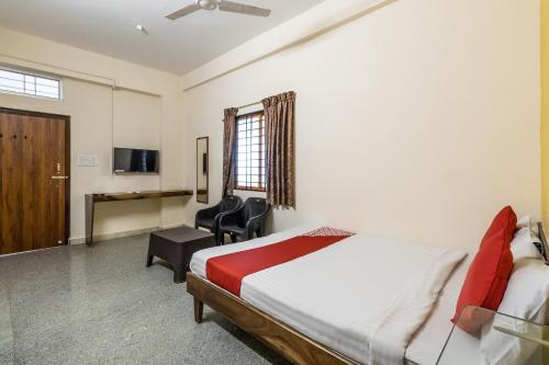 a bedroom with a bed and a desk and chairs at OYO Supriya Lodge in Hassan