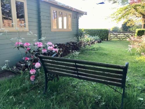 a park bench in front of a house with flowers at Tranquil Norfolk Log Cabin - Stunning Rural Sunset Views in Weston Longville
