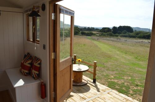 a door to a porch with a table and a field at Under the Stars Shepherds Huts at Harbors Lake in Newchurch