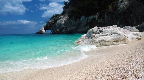 a beach with a large rock in the water at Marina's apartment Ogliastra in Lotzorai