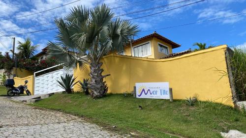a palm tree in front of a yellow house with a sign at MarTito Forno Pousada - Armação dos Buzios in Búzios