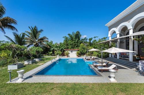 a swimming pool with chairs and umbrellas next to a house at SaffronStays Zuma Villa, Pawna - luxury villa with a heated pool, sports court and gym in Malavli