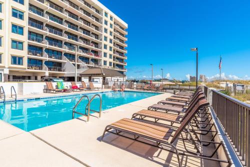 a swimming pool with chaise lounge chairs next to a building at Island Winds East 202 by ALBVR - Beautifully renovated beachfront condo & steps away from Hangout & more! in Gulf Shores