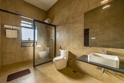 a bathroom with a toilet and a sink and a mirror at SaffronStays Zuma Villa, Pawna - luxury villa with a heated pool, sports court and gym in Malavli