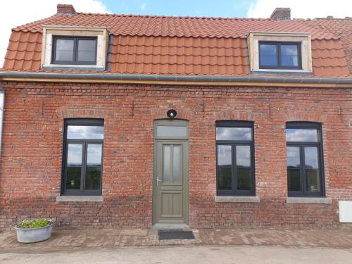 un edificio de ladrillo con una puerta verde y ventanas en Le Moole Veld en Steenbecque