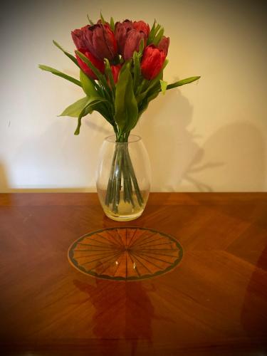 a vase filled with red flowers on a wooden table at Mulberry in Nairn