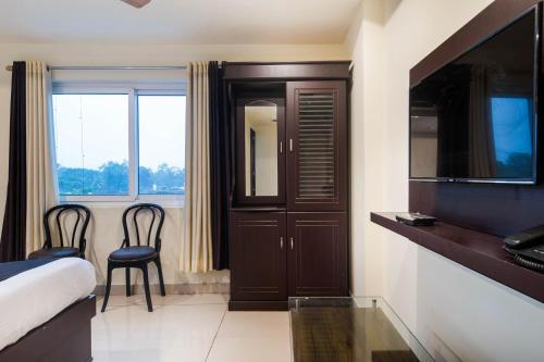 a bedroom with a bed and a tv and a window at Capital O Hotel Alfa in Vijayawāda