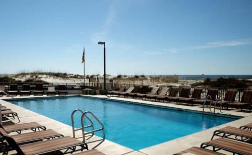a swimming pool with chaises and chairs next to a beach at Island Winds East 308 by ALBVR - Beautifully renovated beachfront condo & steps away from Hangout & more! in Gulf Shores