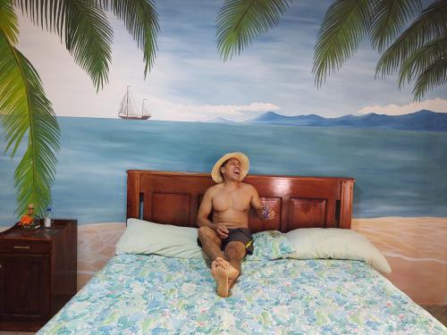 a man in a hat sitting on a bed at Casa Hotel Familiar 