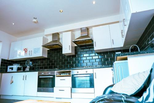 een keuken met witte kasten en zwarte tegels op de muur bij 412b Westgate - Room 6 in Elswick
