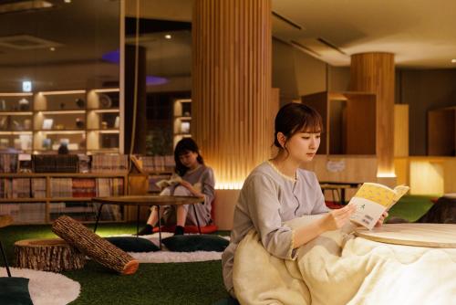 a woman sitting on the floor reading a book at Ashibetsu Onsen Starlight Hotel in Ashibetsu