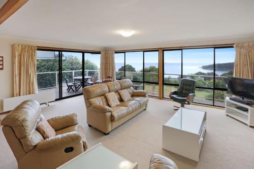 a living room with couches and a tv and large windows at 27 Kanangra Street Pambula Beach in Pambula Beach