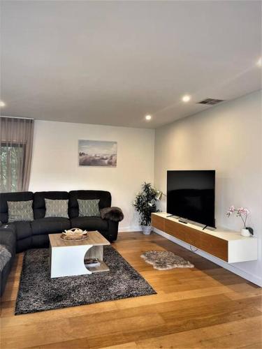 a living room with a black couch and a flat screen tv at Unique 3 Bedroom House close to Merewether Beach in Merewether