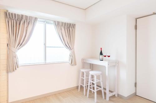um quarto branco com uma janela, uma mesa e bancos em River Side Namba 600 em Osaka
