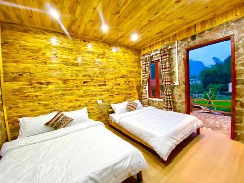 two beds in a room with a wooden wall at Lan Rừng Homestay in Lũng Niêo
