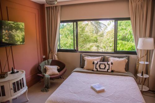 a bedroom with a bed and a chair and windows at Sunset Hilltop Ocean View 2bd House in Haad Tian
