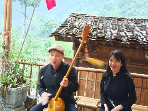 a man and a woman sitting on a porch with a guitar at Quang Thuận Bản Giốc Homestay in Cao Bằng