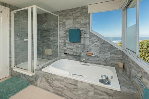 een grote badkamer met een bad en een raam bij Wild Waters at Kraal Rock on the cliffs in Hermanus in Hermanus