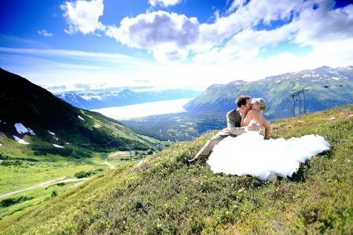 a bride and groom sitting on top of a hill at Alyeska Resort in Girdwood