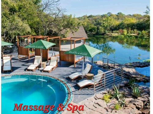 a swimming pool with chairs and umbrellas next to a lake at Spacious Golf & Wildlife Estate in Hartbeespoort 10 sleeper in Hartbeespoort