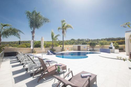a patio with chairs and a pool with palm trees at Villa Margarita in Protaras