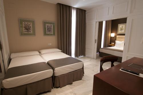 a hotel room with two beds and a desk at Hotel San Gil in Seville