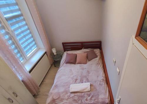 a small bedroom with a bed with pink sheets and a window at Mieszkanie przy zielonej bramie in Gdańsk