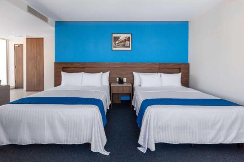 a hotel room with two beds and a blue wall at Wyndham Puebla Angelopolis in Puebla