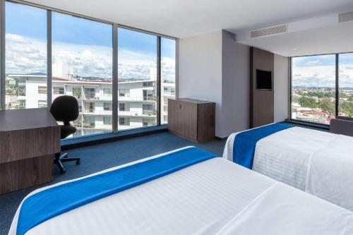 a hotel room with two beds and a desk and windows at Wyndham Puebla Angelopolis in Puebla