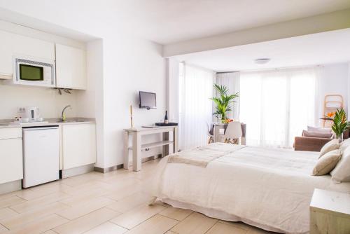 a white bedroom with a large bed and a kitchen at Dunas Club - Hotel & Apartamentos in Corralejo