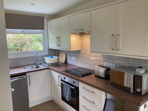 a kitchen with white cabinets and a sink at 13 The Park in Kilkhampton
