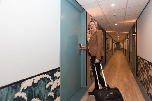 una donna in piedi in un corridoio con una valigia di Beach Hotel I Kloeg Collection a Zoutelande