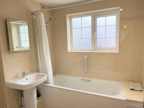 baño con bañera, lavabo y ventana en Le Douit Farm Self Catering, en St Martin Guernsey