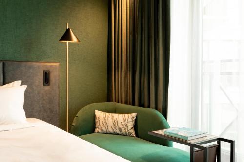 a bedroom with a green chair and a bed and a lamp at The Den, 's-Hertogenbosch, a Tribute Portfolio Hotel in Den Bosch