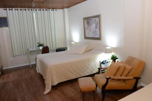 a bedroom with a large bed and a chair and a table at Skalla Hotel Nova Odessa in Nova Odessa