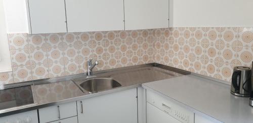 uma cozinha com um lavatório de aço inoxidável e armários brancos em Ferienwohnungen Chesa Clois 24 em Lenzerheide