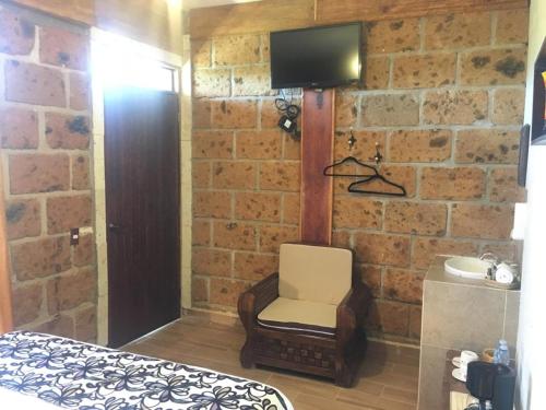 Hotel Real Nirvana في تيكوزاوتلا: غرفة نوم مع كرسي وتلفزيون على جدار من الطوب