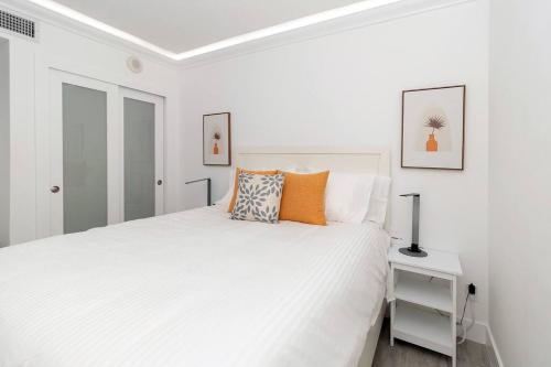 a white bedroom with a large white bed with orange pillows at Stunning & Spacious Resort-Style Condo Across From Beach! in Miami Beach