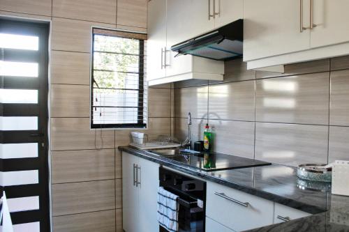 cocina con armarios blancos y encimera negra en Bustani 2 - Self-Catering Studio, en Edenvale
