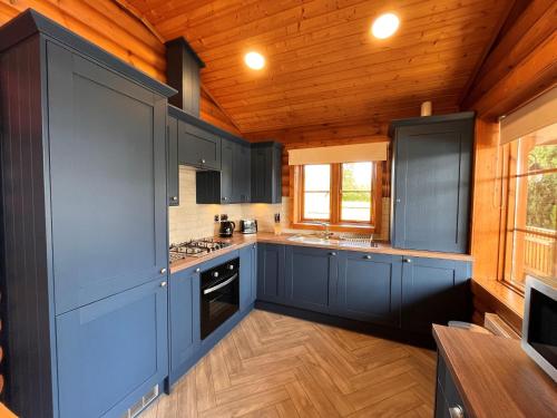 a kitchen with blue cabinets and a wooden ceiling at Countryside Log Cabin With Hot Tub - Beech in Leominster