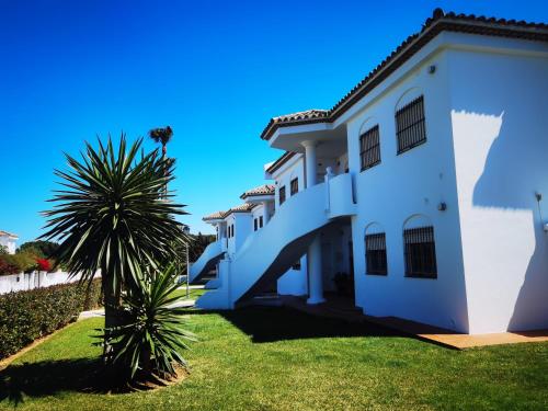 una casa blanca con una palmera delante de ella en LA BARROSA-NOVO SANCTI PETRI, wifi, aire acondicionado, parking, en Chiclana de la Frontera