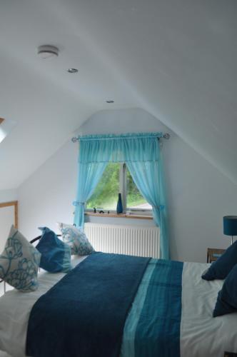 a bedroom with a bed with blue curtains and a window at Meadow Oak Accommodation in Bodmin