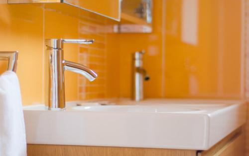 a sink in a bathroom with an orange wall at Flats - Duna Parque Group in Vila Nova de Milfontes