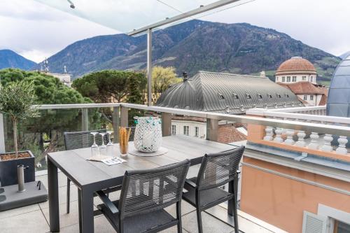 a table and chairs on a balcony with mountains at Luxus Penthouse mit Terrasse, Garage, Fahrradraum und Infrarotsauna in Merano