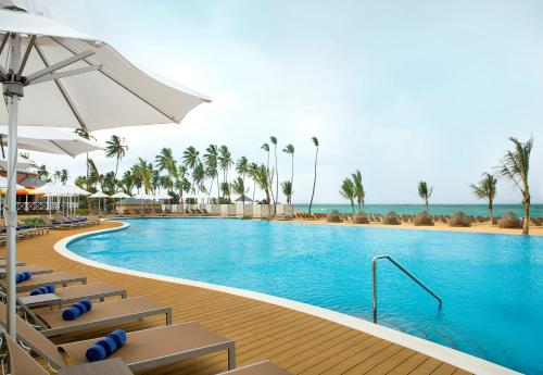 a swimming pool with chairs and an umbrella and the ocean at Nickelodeon Hotels & Resorts Punta Cana - Gourmet All Inclusive by Karisma in Punta Cana